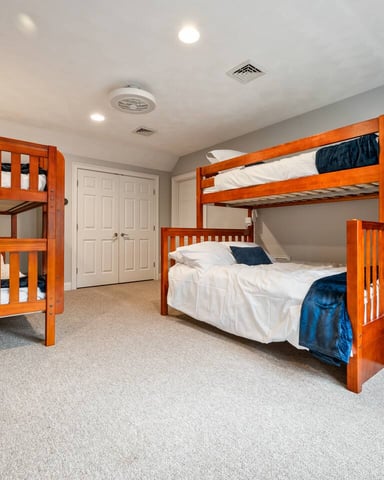 Bedroom with two wooden bunk beds, one queen bed with blue bedding, white closet doors, and beige carpet.